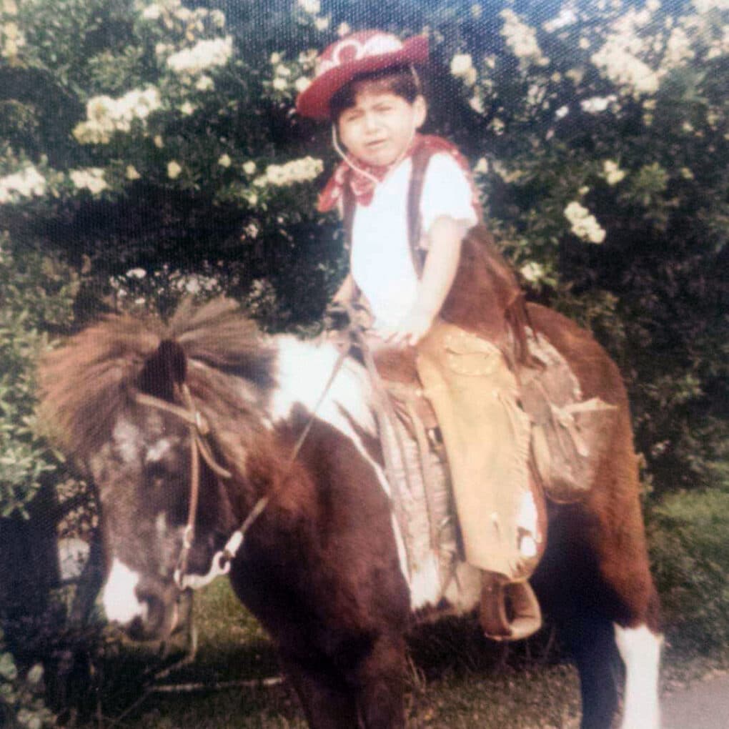 Child on a pony, wearing cowboy outfit.