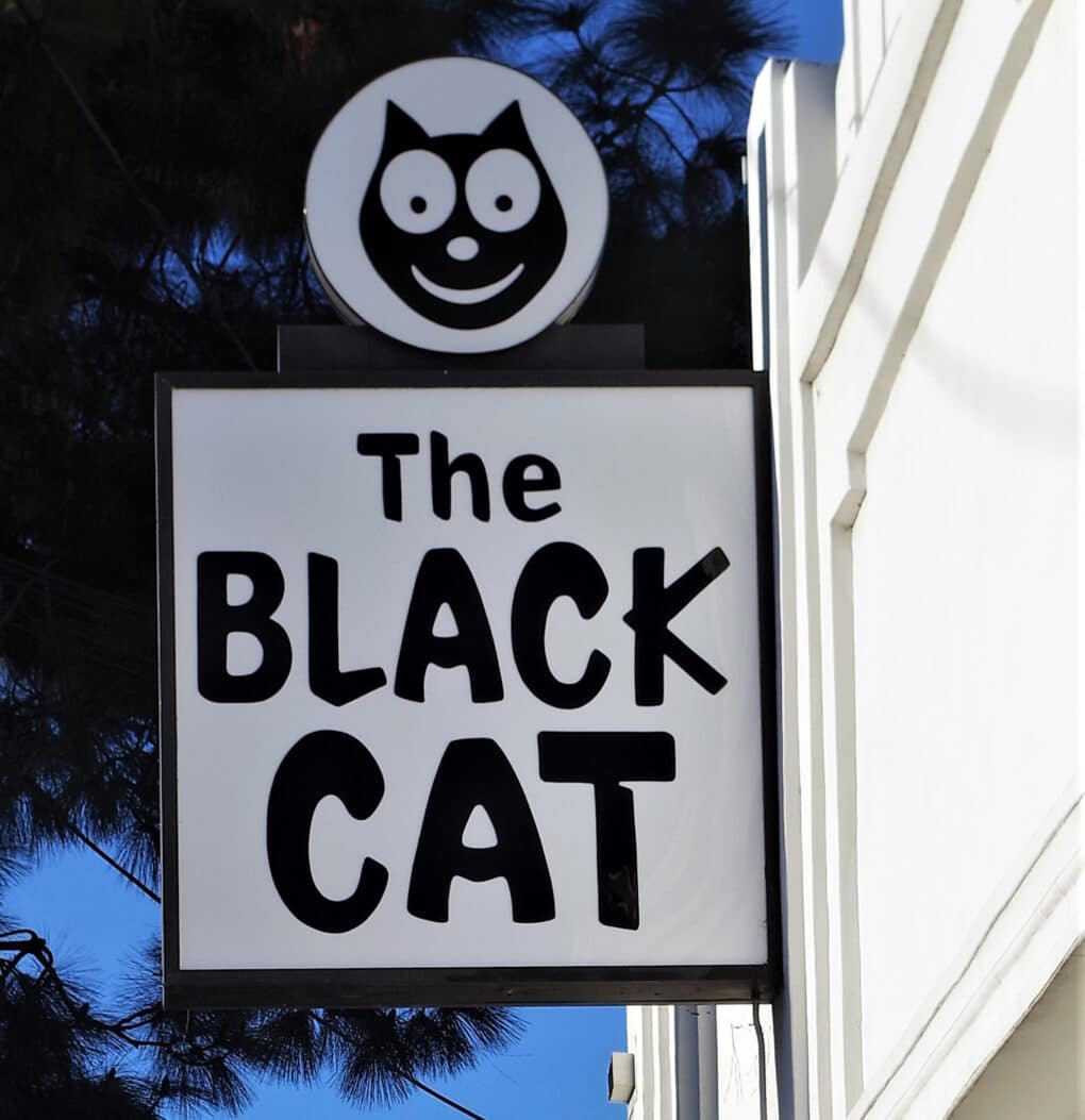 Sign for Black Cat Tavern against blue sky.