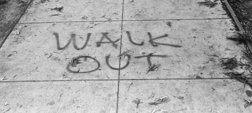 The words WALK OUT spray-painted on the sidewalk.