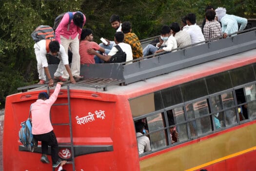A man climbing onto the roof of a bus, being helped by others already at the top.