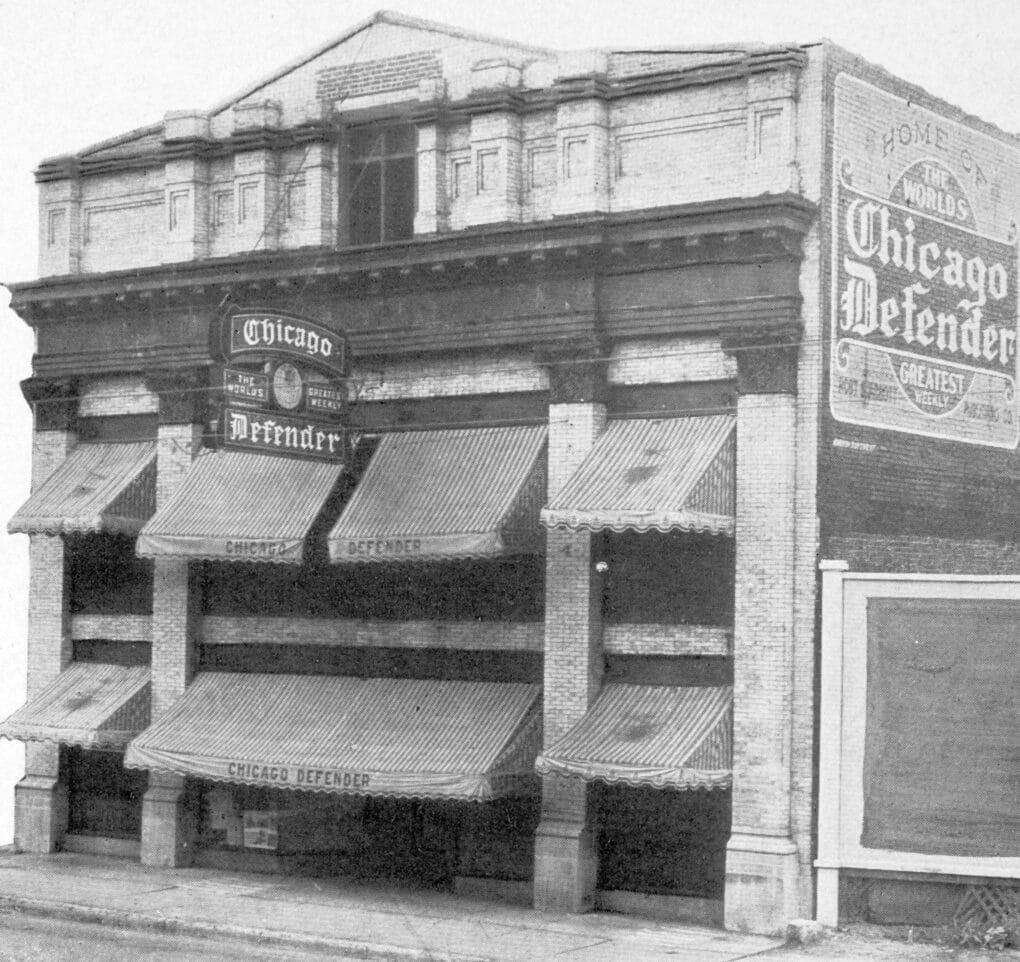 Black and white photograph of three story building with awnings and sign reading CHICAGO DEFENDER.