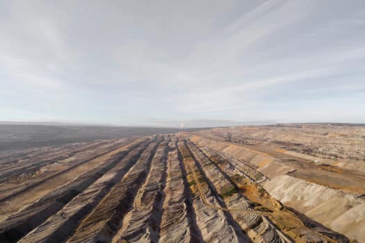 Parallel machine-made trenches running to the horizon. A plume of smoke visible at the horizon line.
