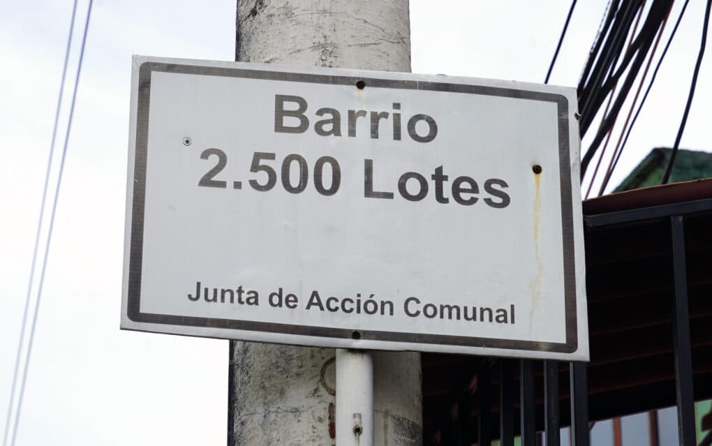 Street sign reading "Barrio 2.500 Lotes--Junta de Acción Comunal"