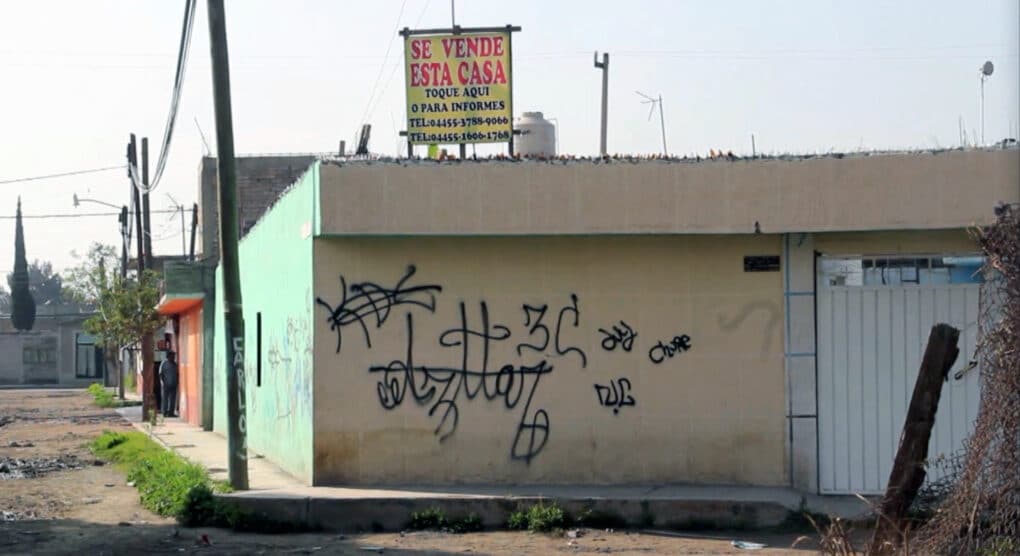 A small graffitied building with a sign on the roof saying "Se Vende Esta Casa."