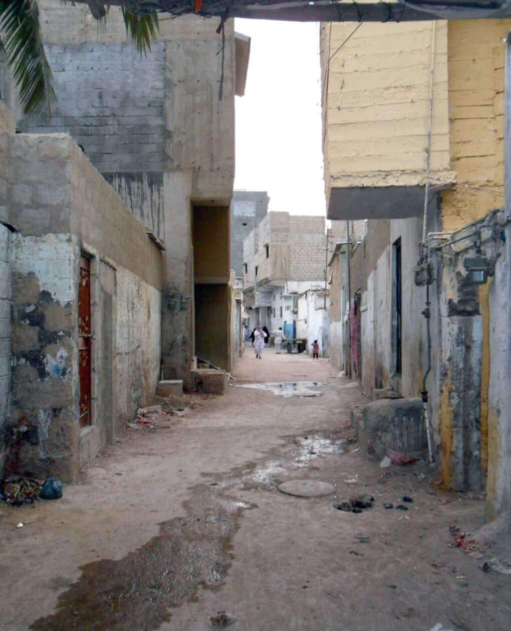 Narrow unpaved street closely built with concrete structures on each side.