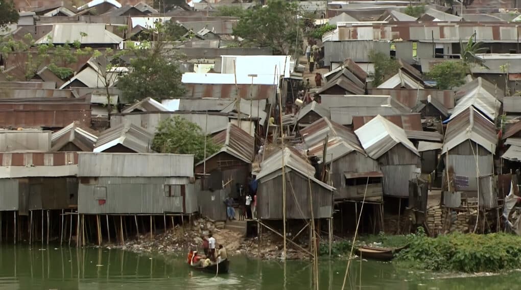 Elevated view of closely built shacks on stilts beside a waterway.