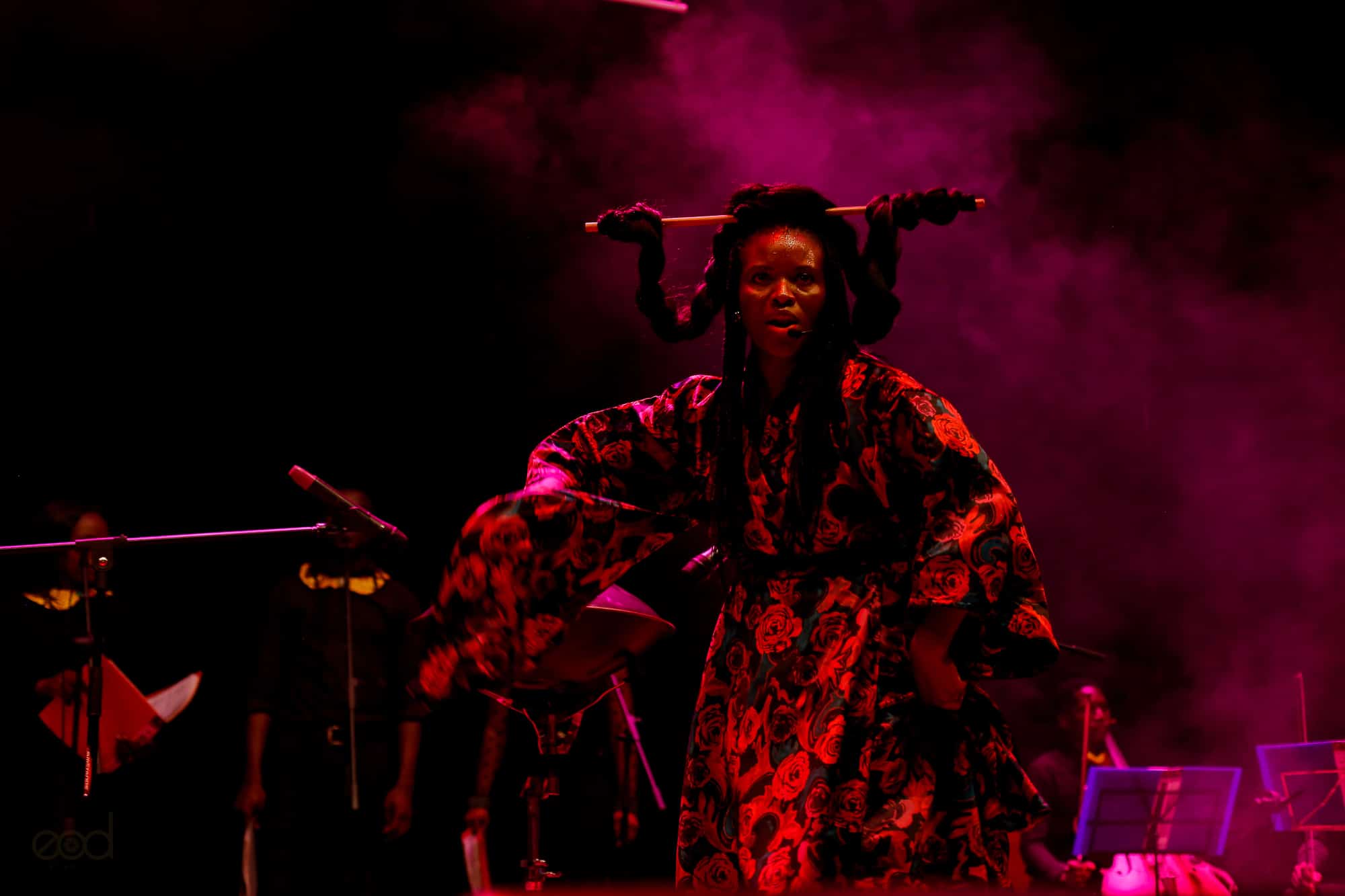 Click to Enlarge Black performer onstage in dramatic red light.