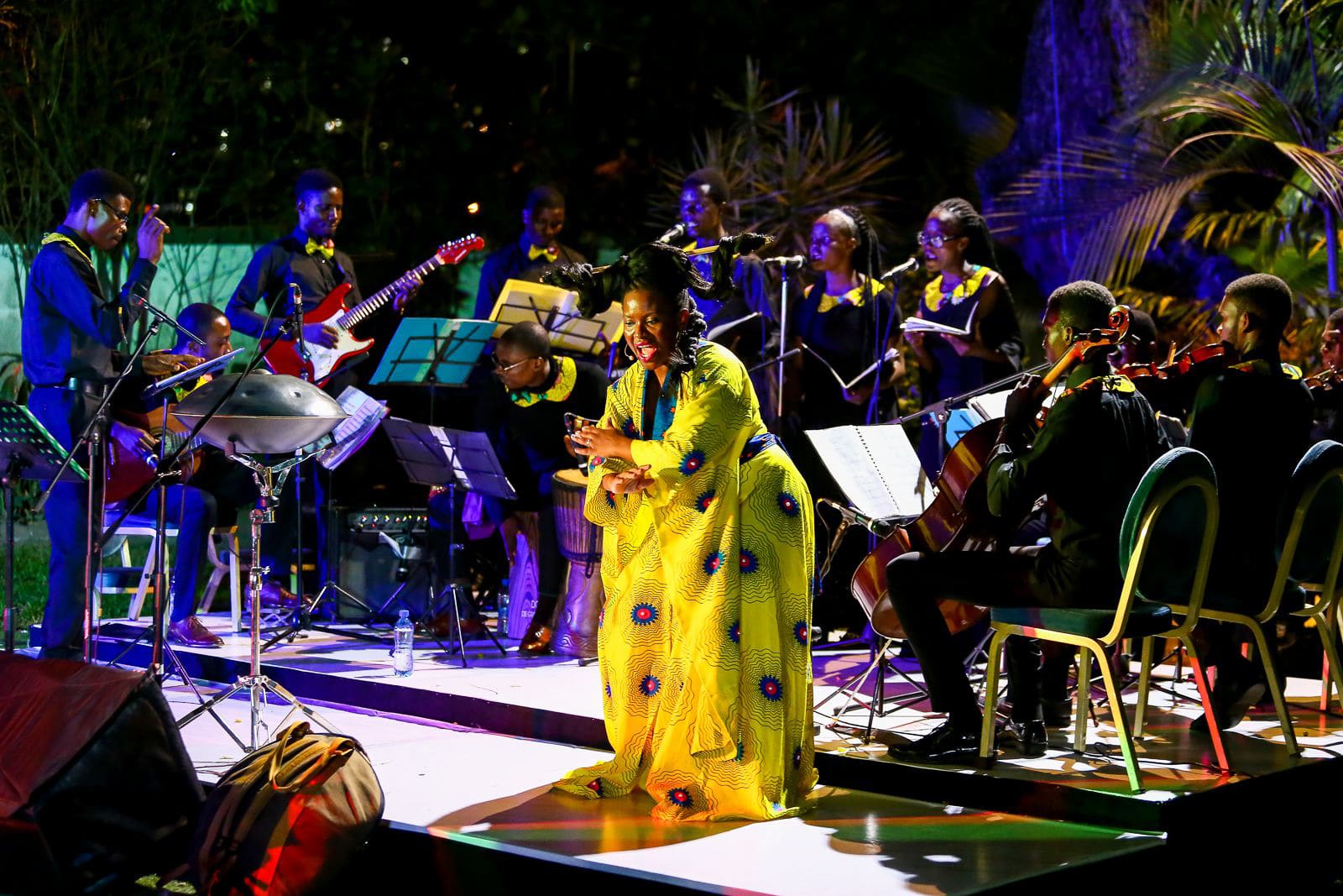 Click to Enlarge Black woman in bright yellow dress singing on stage, surrounded by Black orchestra.