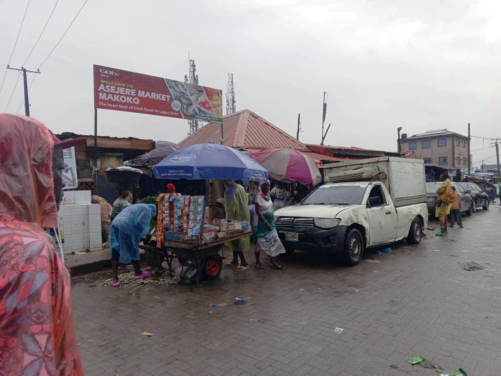 Click to Enlarge A kiosk and pick-up truck in front of the local market, with people moving about.