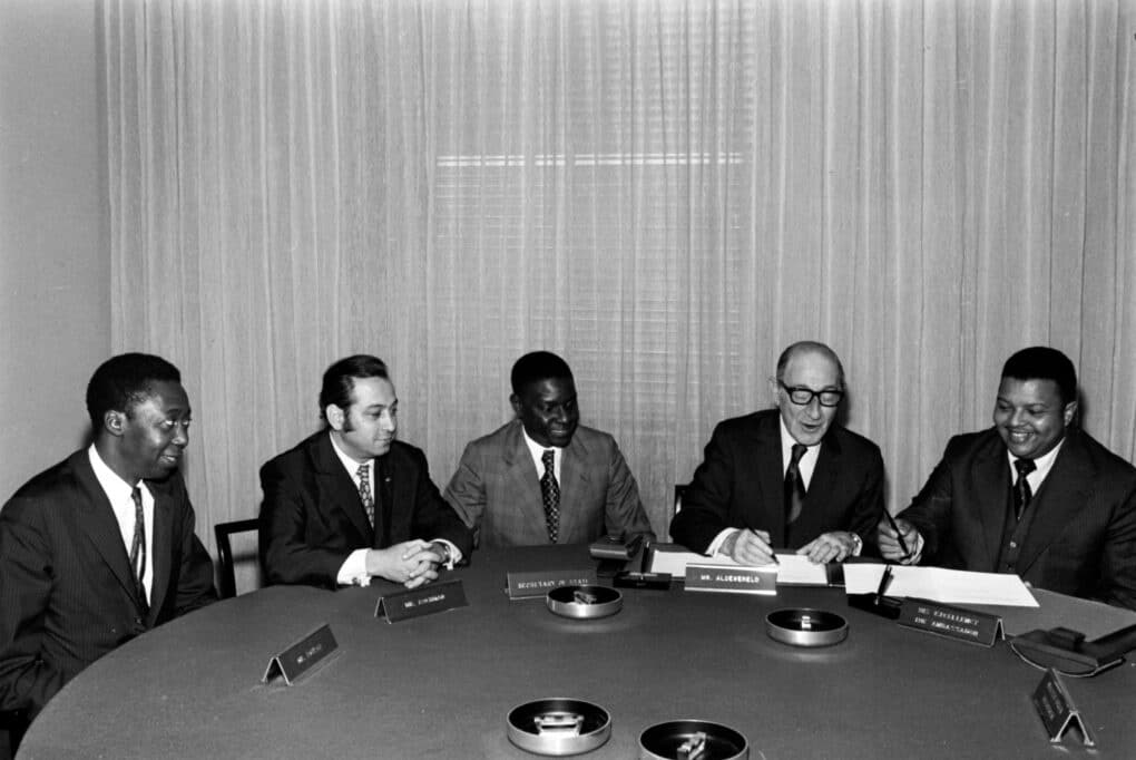 Black-and-white photograph of five men, three Black and two white, seated at a conference table.