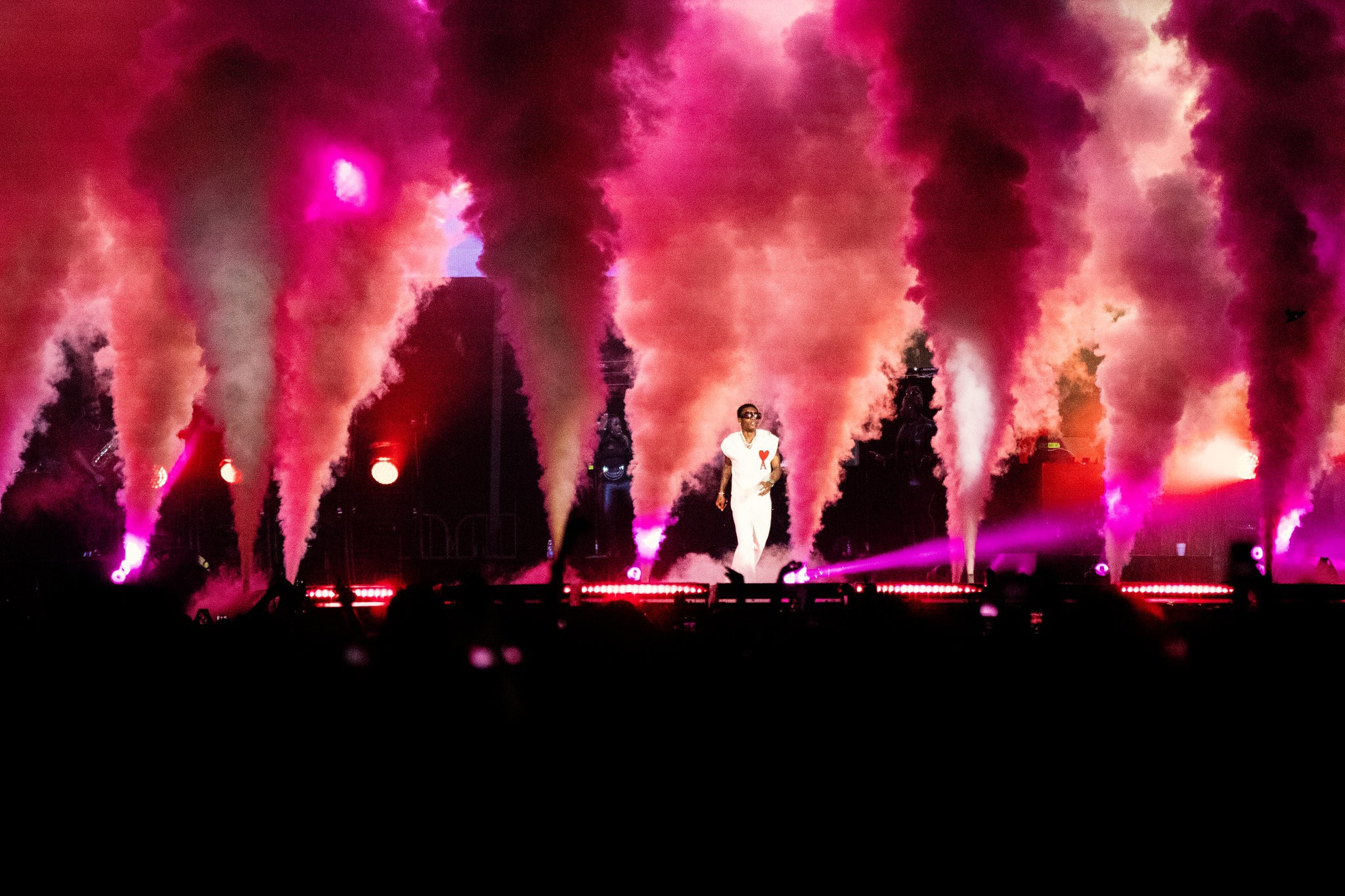 Click to Enlarge Performer in white jumpsuit onstage amidst plumes of pink smoke.
