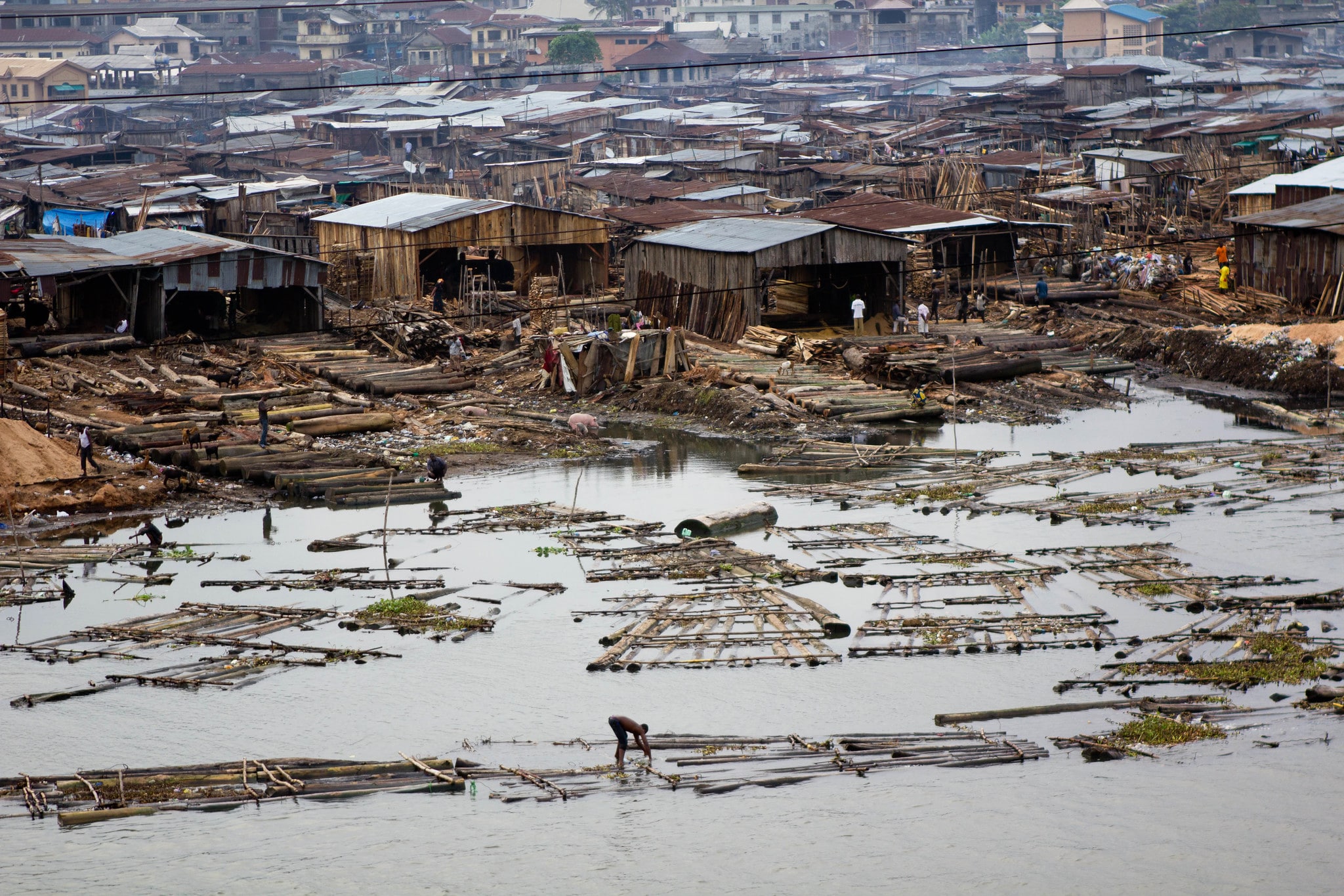 Click to Enlarge A view from above of men building wooden platforms in the water. In the background, the already-developed parts of Makóko.