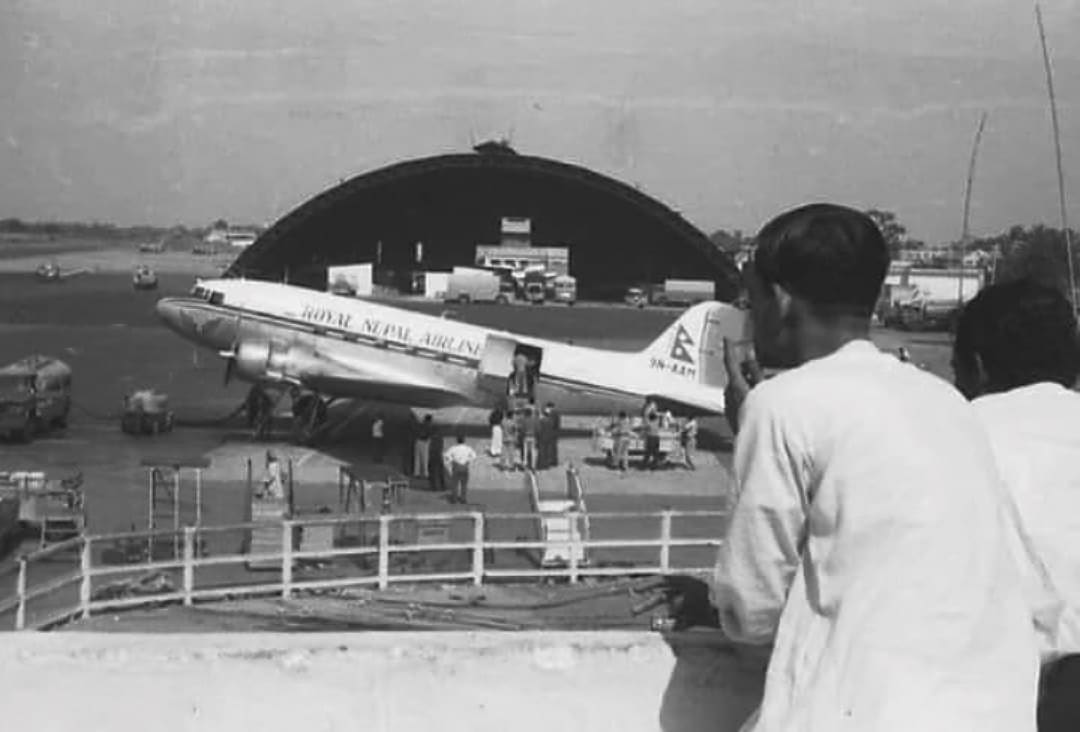 Click to Enlarge Black-and-white photograph of two men watching a Royal Nepal Airlines jet load or unload.