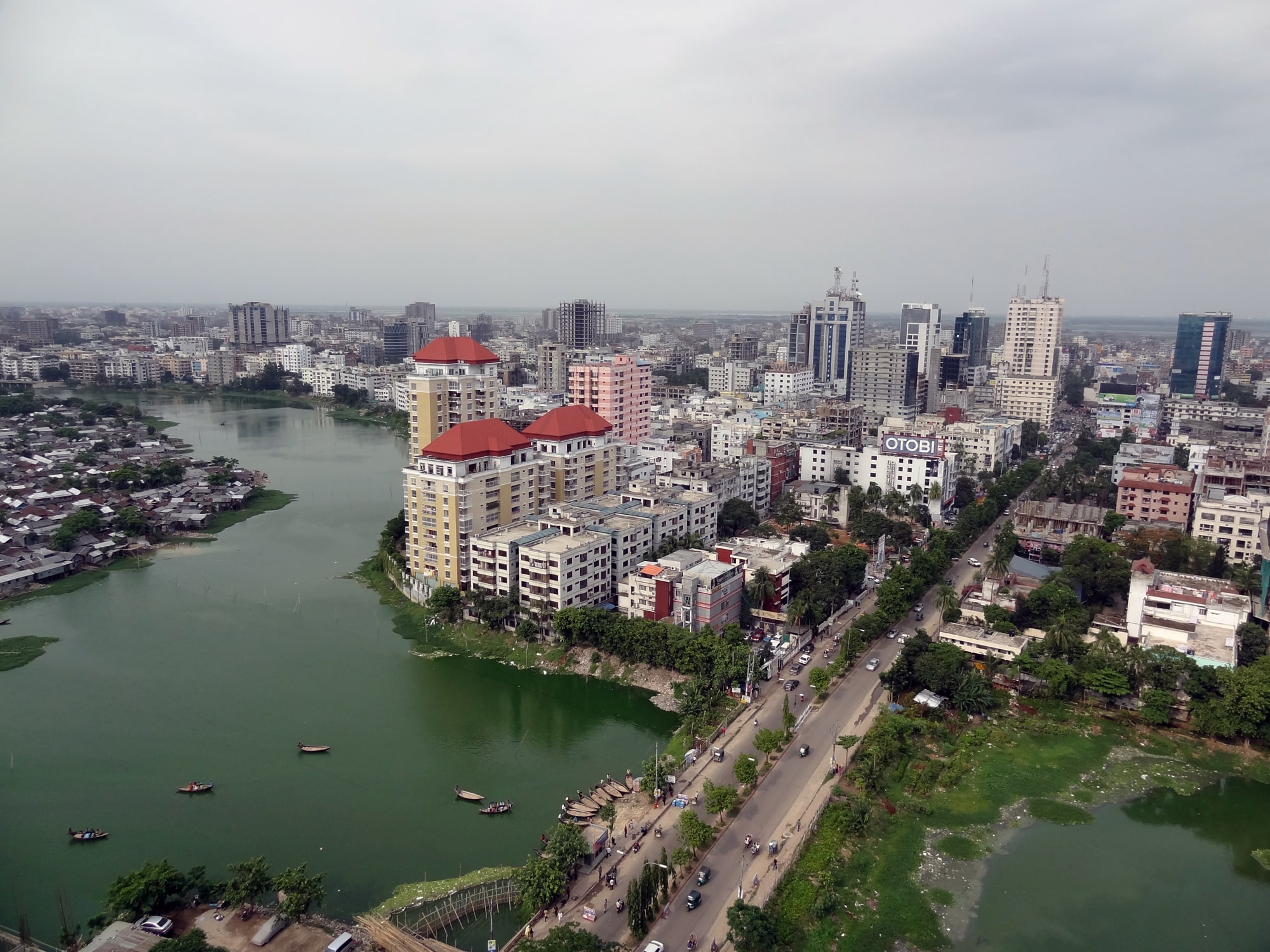Click to Enlarge Photo from an elevated perspective showing boulevard over water body leading into densely built neighborhood of housing blocks and office towers.