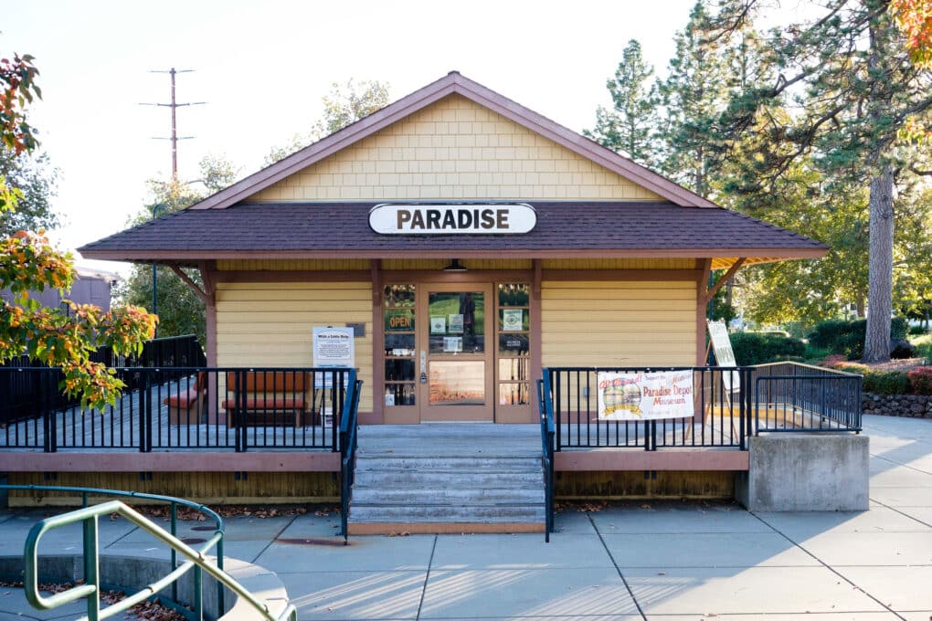 Color photograph of small-town city hall with the word PARADISE above the door, and pine trees behind the building.
