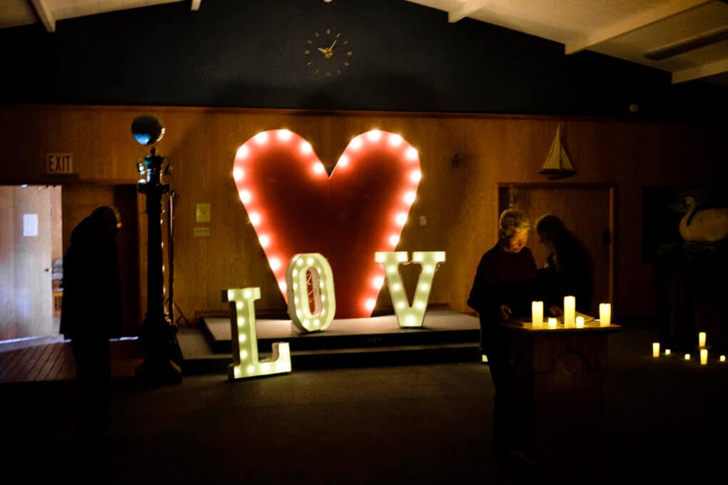 Color photo of large heart-shaped shrine in a darkened municipal hall, with large letters spelling out LOV (the E is not visible).