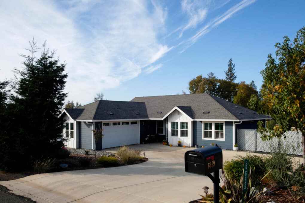 Color photo of brand new gray-and-white ranch-style house with a large concrete apron and driveway.