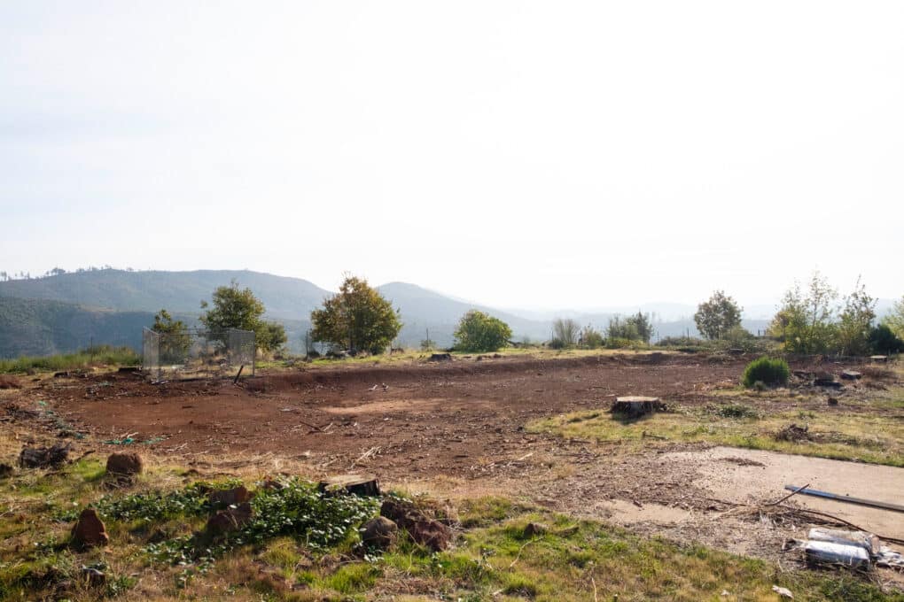 Color photograph of red-dirt vacant lot with large hills in the background.
