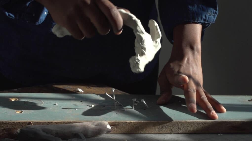 A second still from the film Reparation Hardware, showing a deformed, unusable clay hammer being used to hammer in crooked nails.