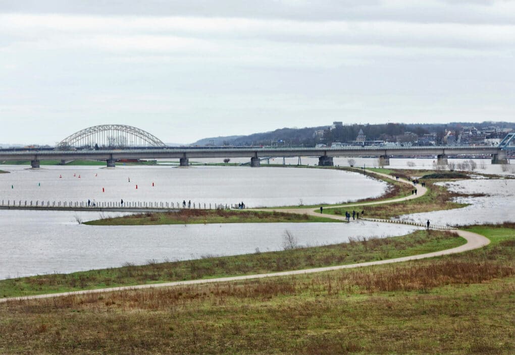 Landscape photo showing a wide river with two channels separated by a narrow island where people are walking.