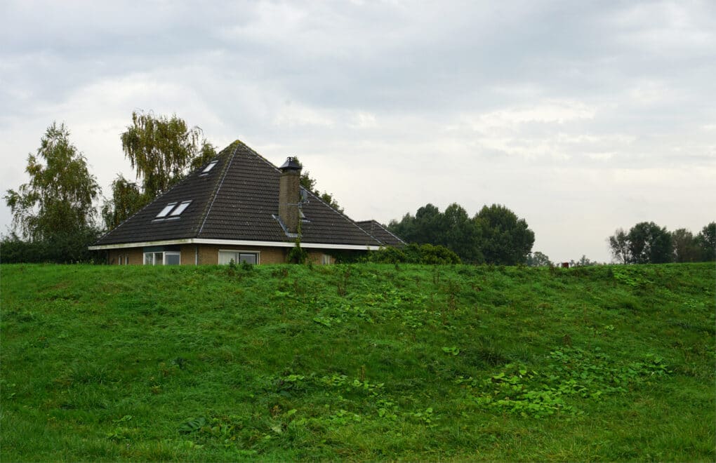 House obscured behind a grassy mound. Only the roof is visible.