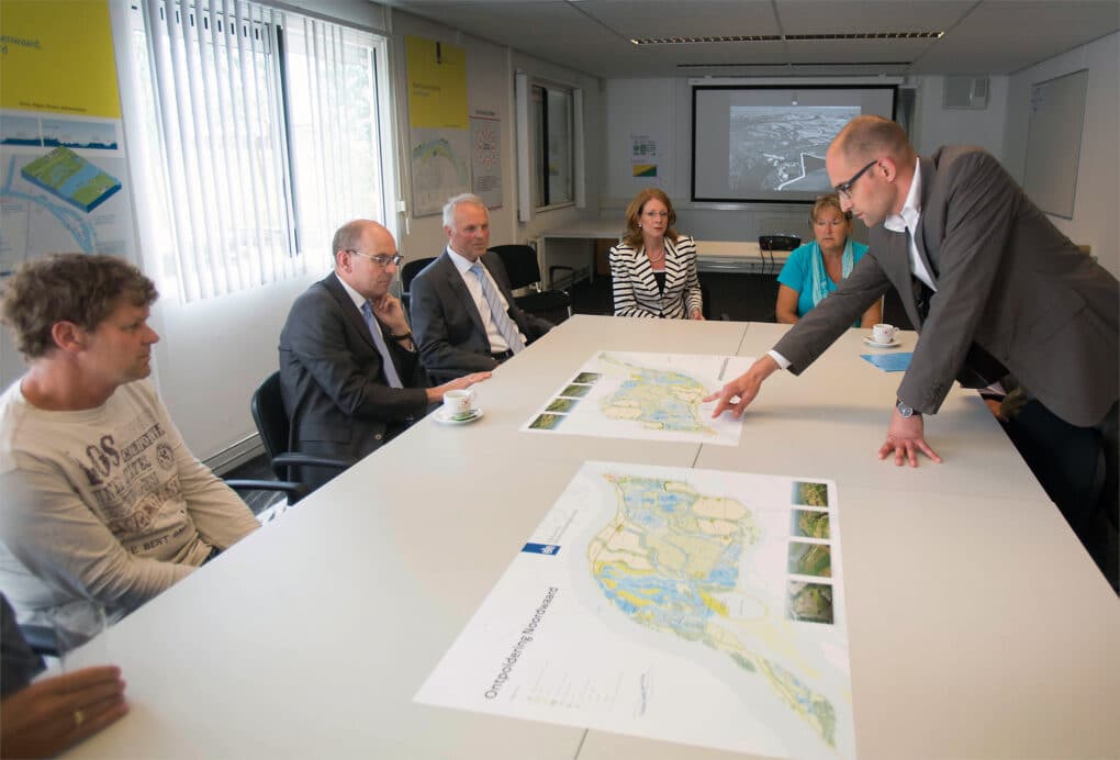People in suits and others dressed more informally, sitting around a conference table looking at a plan of the Depoldering Noordwaard project.