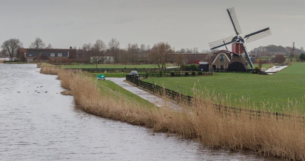 Windmill in agricultural fields next to a canal that is flowing at a higher elevation than the fields