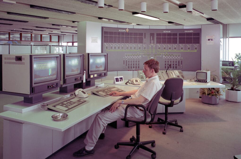 Man sitting in front of three computer monitors in a control room.