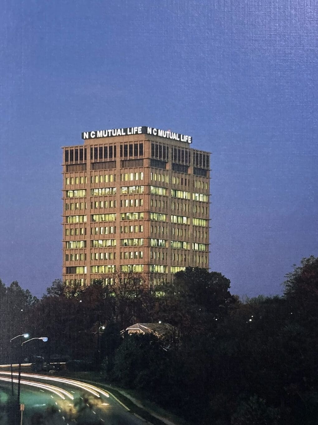 Color photograph of a concrete tower, with the words NC MUTUAL LIFE illuminated at the top.