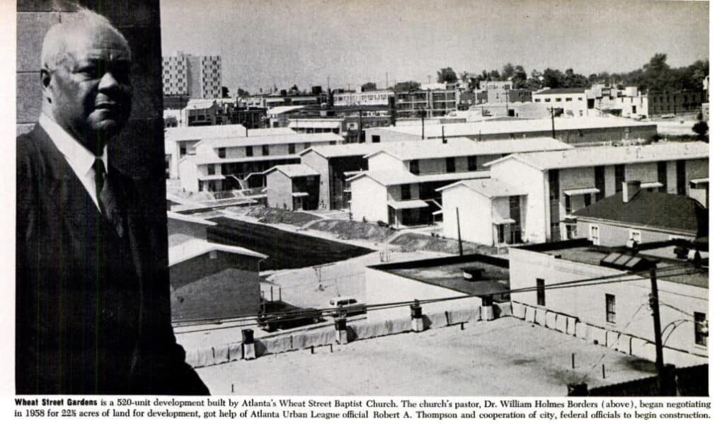 Black and white photograph of black business man looking out over a new development of low-rise housing blocks.