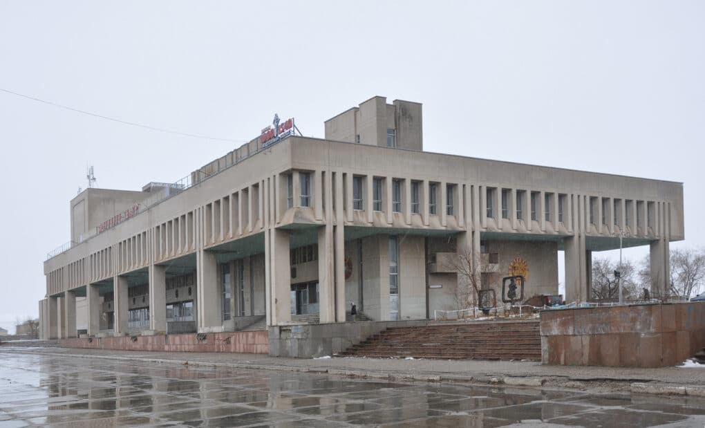 Color photograph of brutalist concrete building in rainy paved plaza.