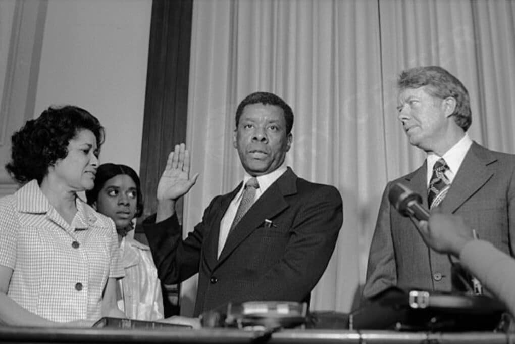 A black business man holding up his hand to swear an oath, while President Jimmy Carter, a black woman, and a black teenaged girl look on.