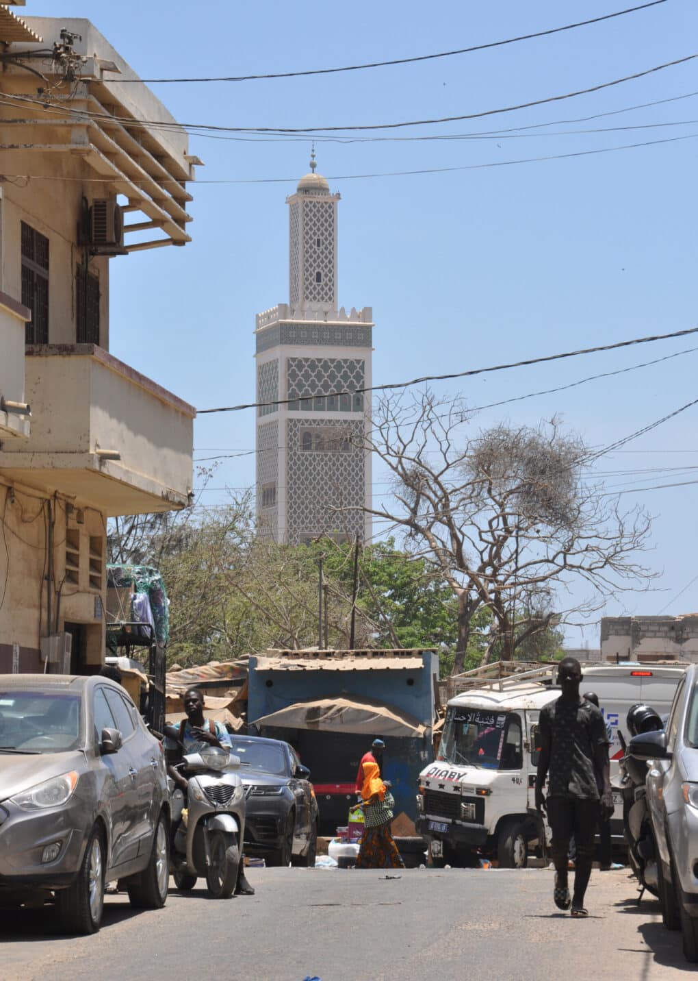 Color photograph of white filigree minaret at the end of a busy city street.