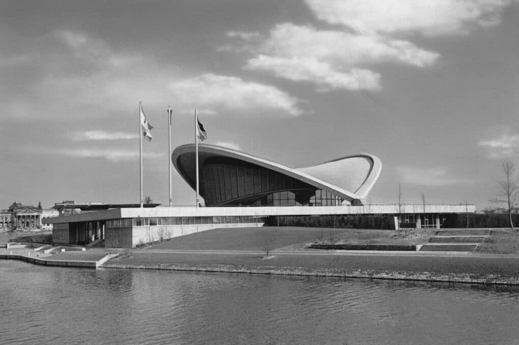 Black-and-white photograph of civic building with shell-like concrete roof and glass walls.
