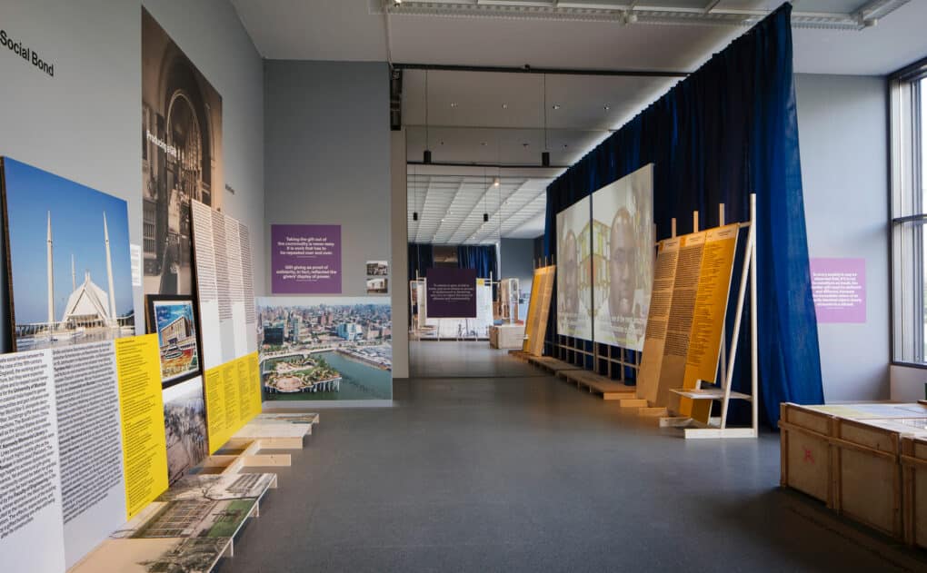 Color photograph of exhibition interior, with text and photo panels leaning against the walls and laid out on low shelves.