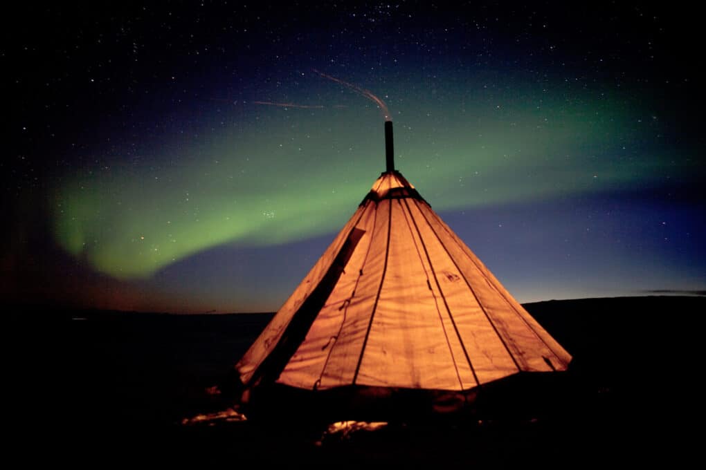 Color photograph of teepee lit from within, glowing against dark sky. 