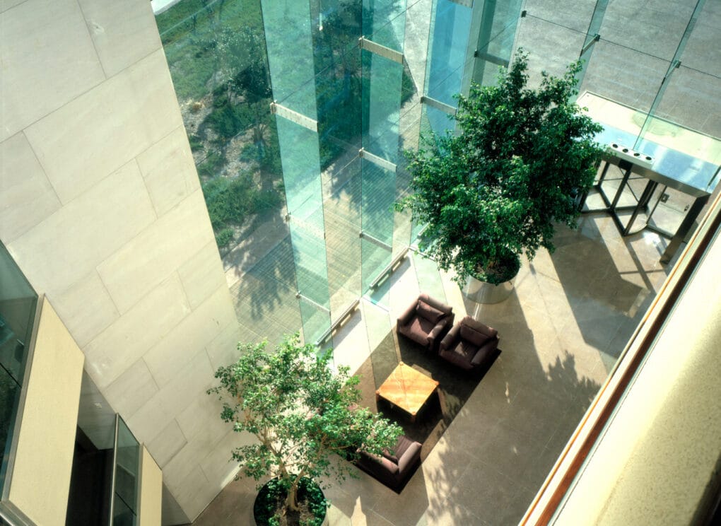 Color photograph of glass-walled space with trees and seating, photographed from above.