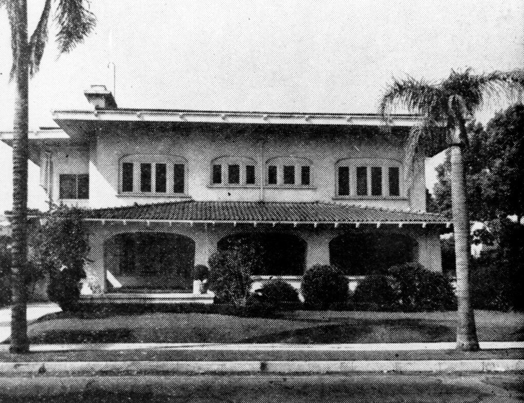 Black-and-white newspaper photograph of large Los Angeles house surrounded by palm trees.