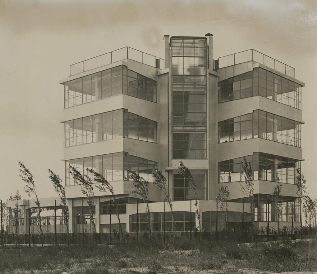 Tall five-story building with two wings, with floor to ceiling windows on every floor and on three sides of each wing.