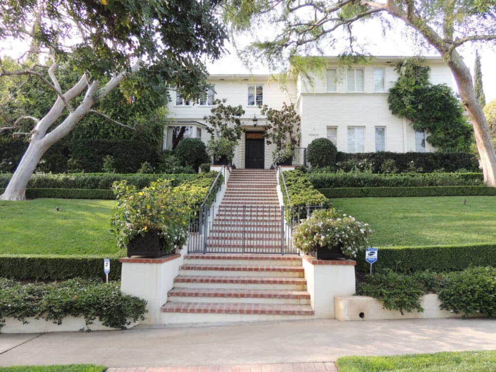 Large home up grand staircase with manicured lawn, painted white.