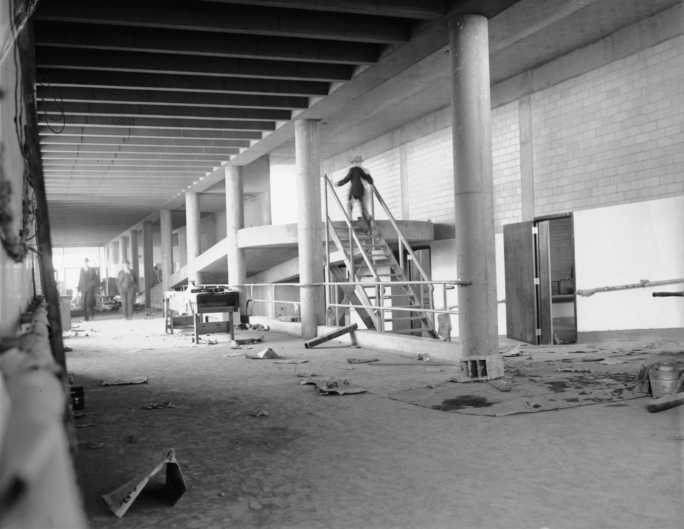Click to Enlarge Interior of building under construction, with structure mostly complete and debris on ground. Men in suits and bowler hats are inspecting.