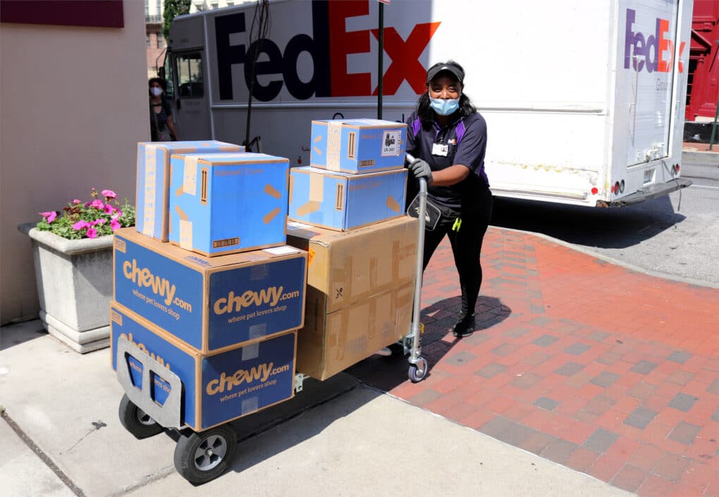A FedEx delivery person pushes a handcart with a dozen big cardboard boxes from major brands, including Chewy.