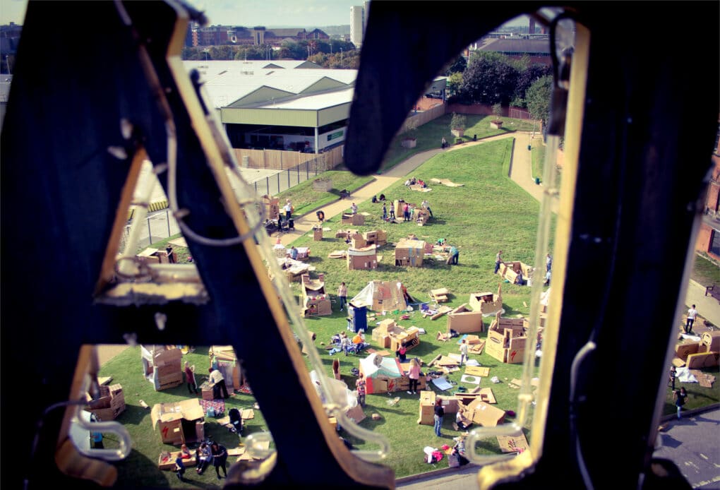 A distant view of dozens of cardboard structures on a grass lawn.