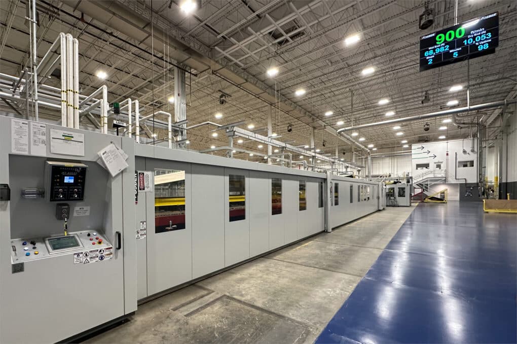 A factory floor, clean and sterile, with a long machine enclosed behind grey metal walls and glass windows.