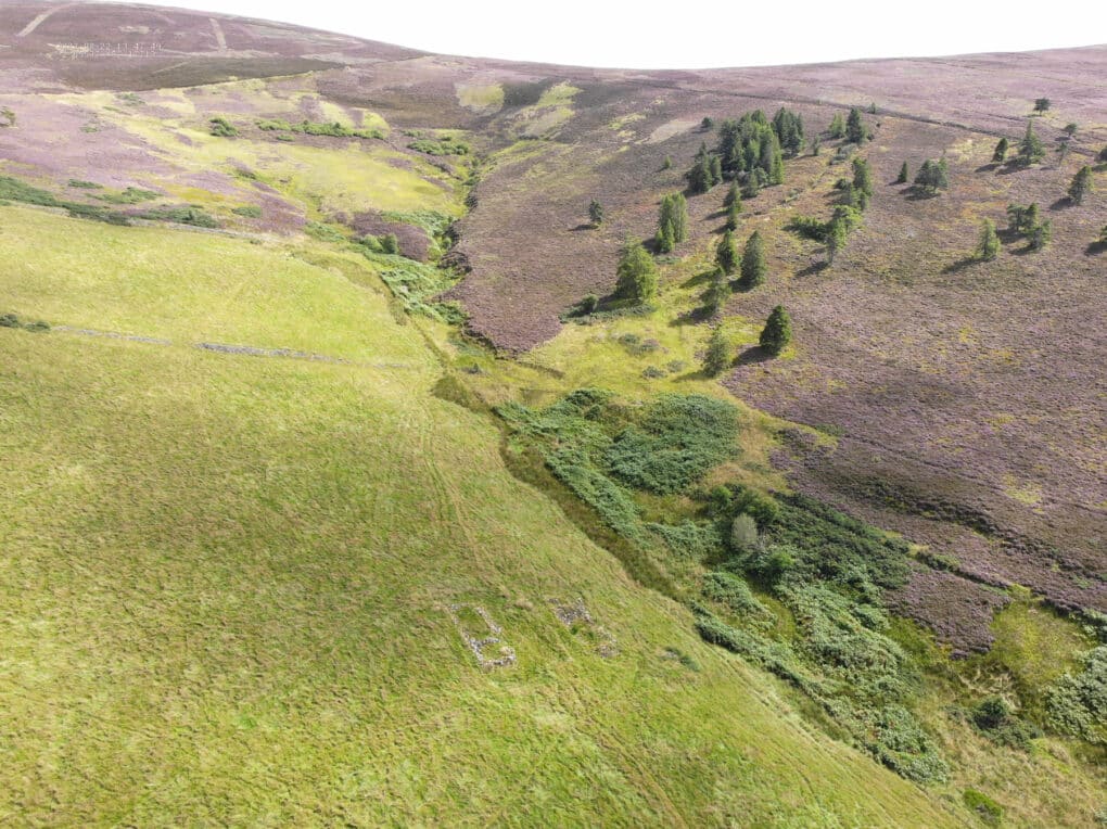 Drone photograph showing green valley with faint outline of stone foundations.
