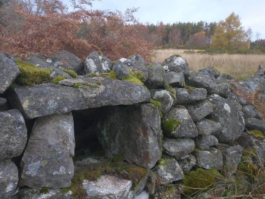 Color photograph of gray stone wall with small stone niche built with heavy single slabs as lintel and sides.