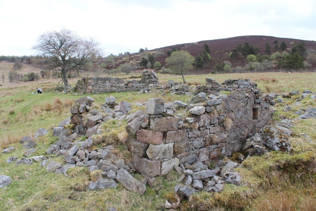 Color photograph of field and hill with ruined foundations of small stone buildings.