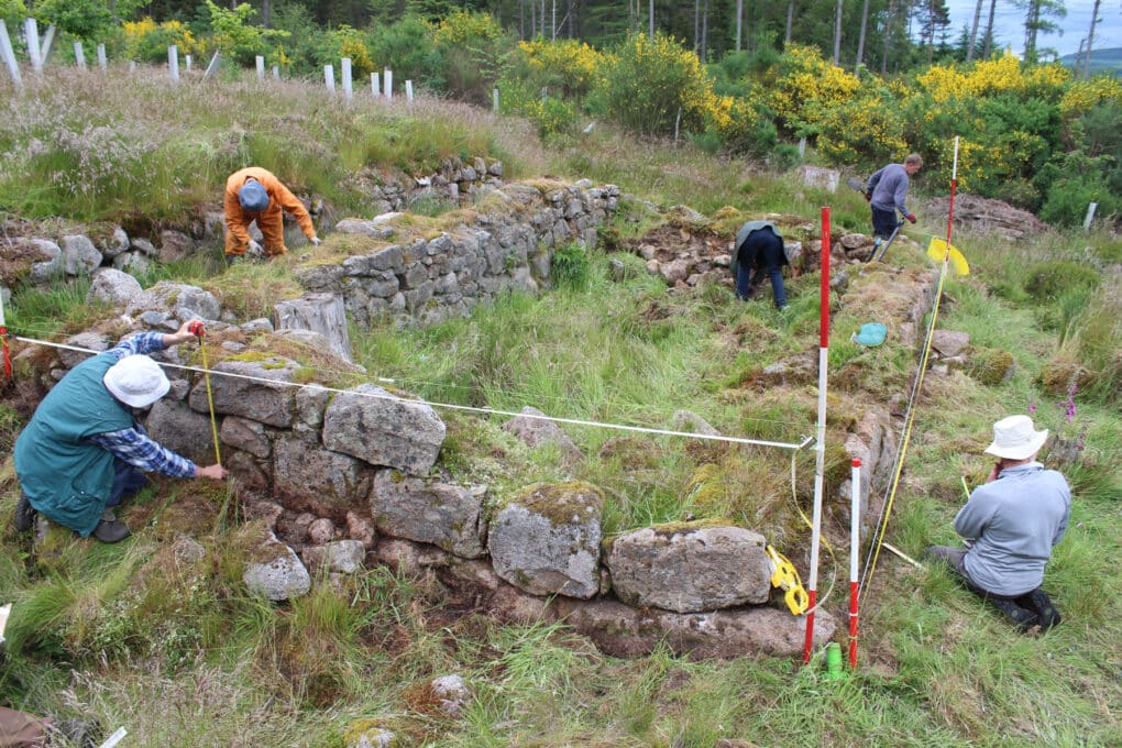 Color photograph of five-person archeological team measuring foundation of a small, ruined stone building.