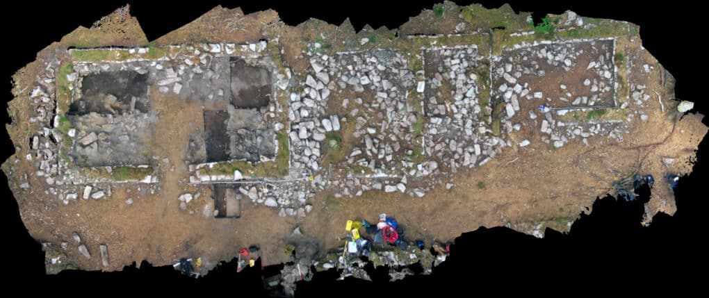 Composite color drone photograph of five small interconnected stone buildings.