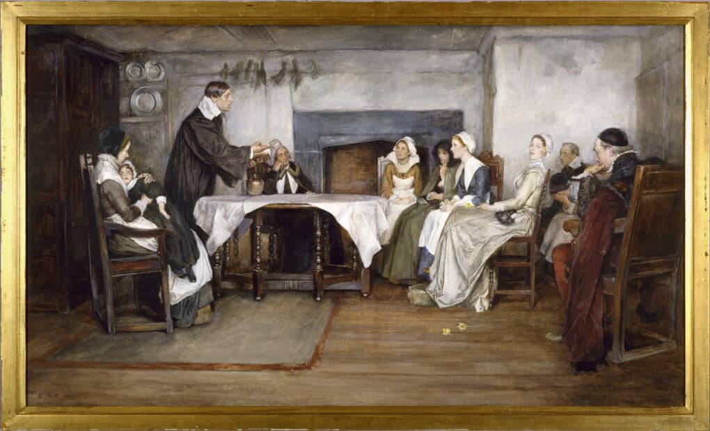 Painting in gold frame showing Puritan family of five women, two men, and a femaile child gathered around a kitchen table, being taught by a Puritan minister.